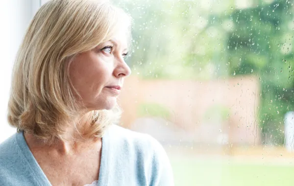 Foto mujer mediana edad mirando con tristeza a través de una ventana con gotas de lluvia