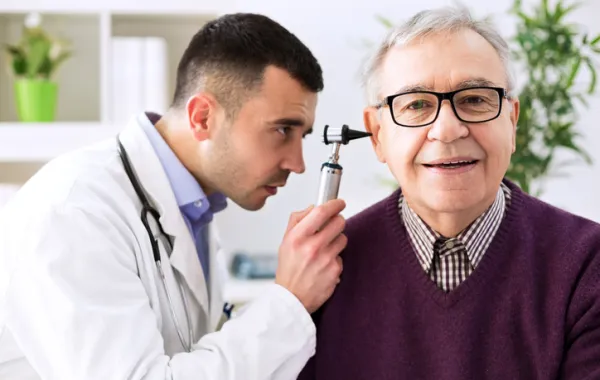Foto de un médico observando el interior del oído de una hombre mayor