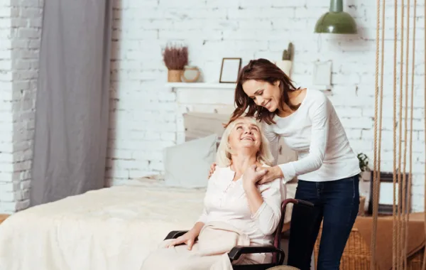 Foto de una mujer en silla de ruedas acompañada por una mujer joven que la atiende
