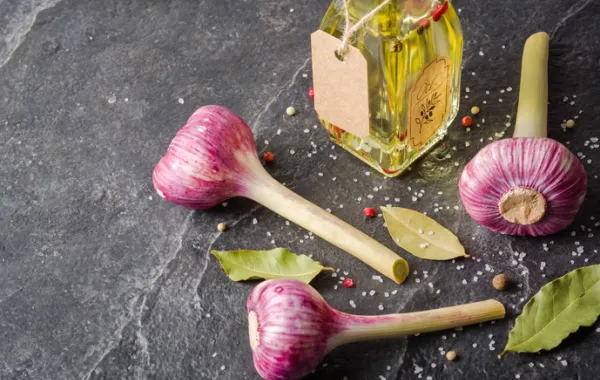 Foto con varias cabeza de ajos de color morado y una botella de aceite de cristal