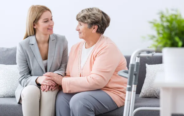 Foto mujer mayor sentada y acompañada por mujer joven que le sonríe