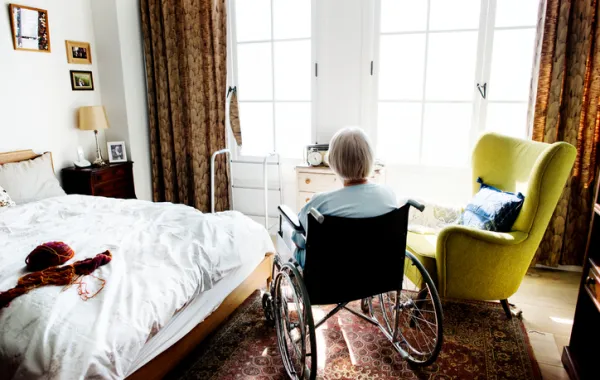 Foto de mujer de espaldas sentada en silla de ruedas en un dormitorio