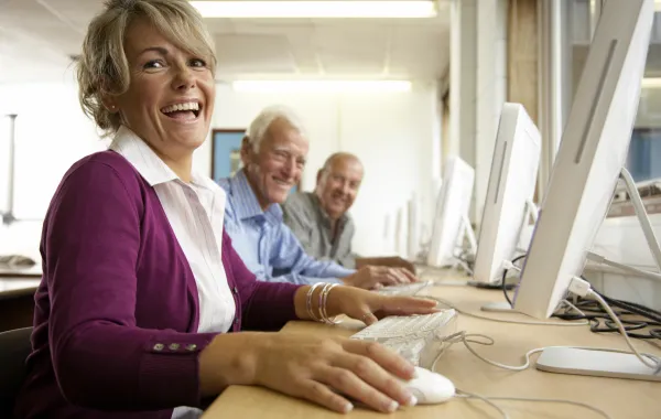 Foto de personas de 60 años delante de un ordenador y sonriendo