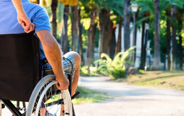 Foto de personas sentada en sillas de ruedas de espaldas y empujada por una persona