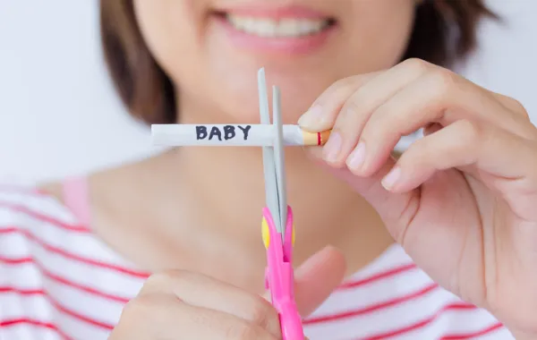 Foto de mujer cortando con tijeras un cigarrillo que tiene escrito bebé