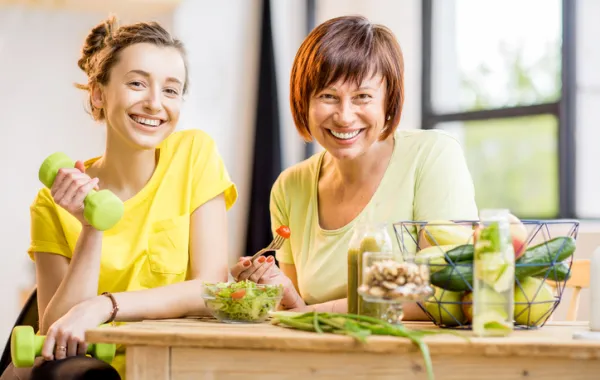 Una madre y una hija sonríen delante de una mesa con verduras