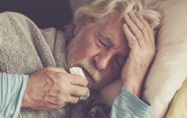 Hombre mayor abrigado en la cama con un pañuelo. Gripe A.