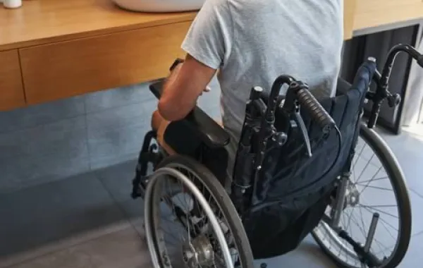 Un hombre en silla de ruedas se lava los dientes mirándose al espejo del baño