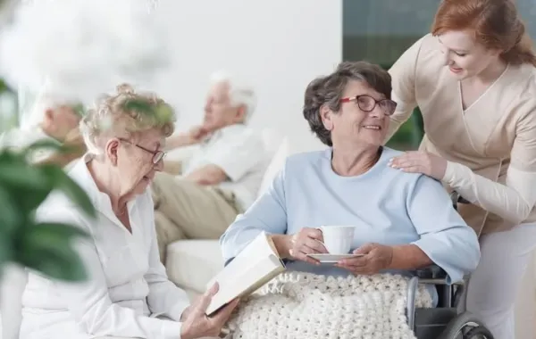 Mujer mayor en silla de ruedas atendida y acompañada de otras 2 mujeres