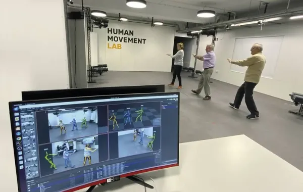 Monitorización del movimiento de tres personas mayores en un entorno de pruebas. En la pared el texto Human Movement Lab.