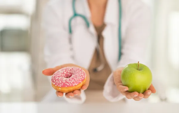 Foto de un médico que sostiene en una mano una manzana y en otra un dulce