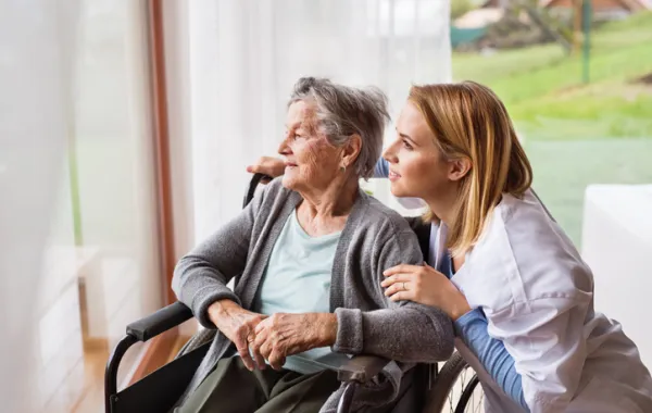 Foto de señora mayor sentada en silla de ruedas acompañada por una enfermera