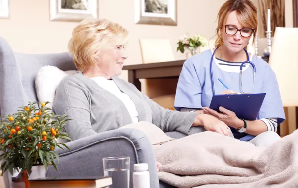 Foto de una mujer mayor sentada y acompañada por un doctora