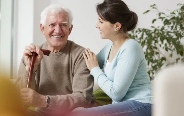 Foto de un hombre anciano sentado y acompañado por un cuidadora joven