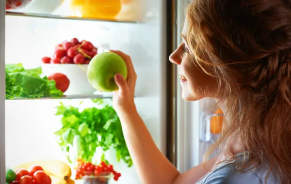 Foto de una mujer joven abriendo una nevera que contiene verduras y frutas