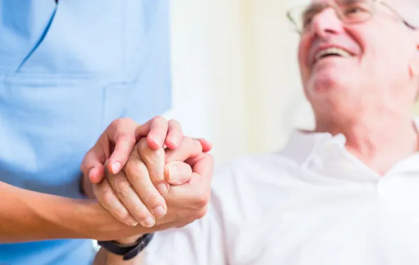 Foto de un señor mayor acompañado por un sanitario que le tiende la mano