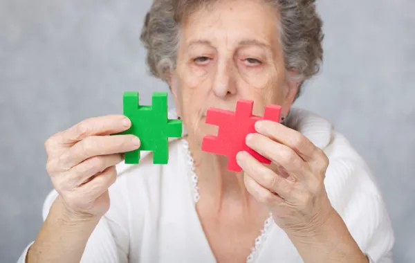 Foto de mujer mayor que mira unas piezas de puzzle sin poder encajarlas