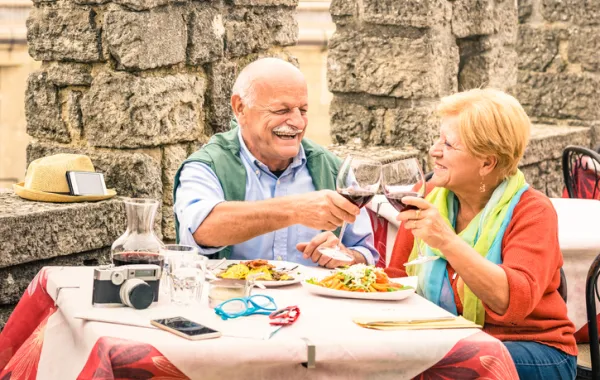 Foto pareja personas mayores sentados en una mesa comiendo y brindando