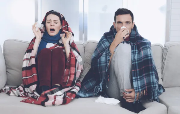 Foto de una pareja sentada en un sillón con síntomas de gripes