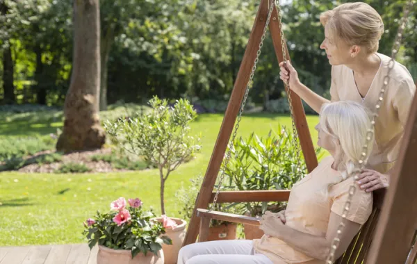 Foto de una mujer mayor sentada en un jardin y acompañada por una mujer joven