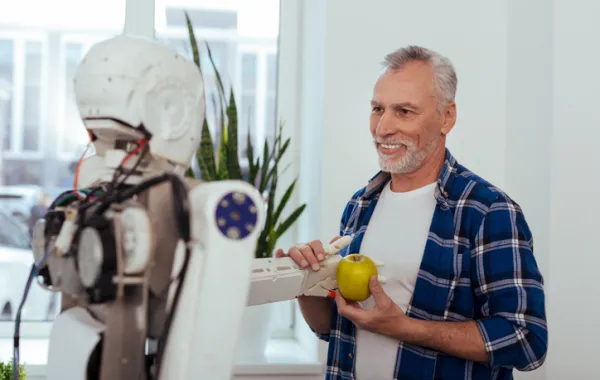 Foto de hombre maduro acompañado de un robot que le ofrece una fruta