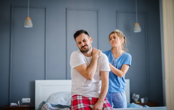 Foto de hombre joven con dolor en un hombre y que le asiste una enfermera