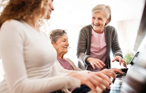 Foto de dos mujeres mayores sentadas delante de un piano acompañadas por una mujer joven