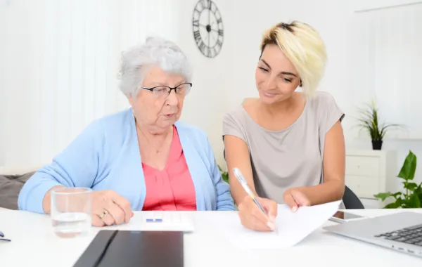 Foto de una mujer mayor acompaña por una asistente social