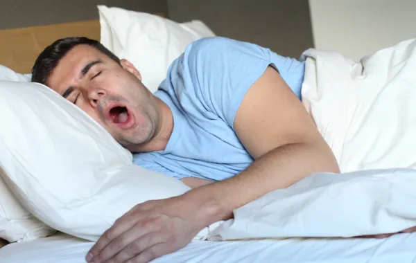 Foto de un hombre tumbado en la cama que bosteza porque no puede dormir