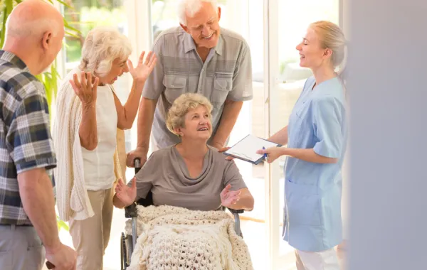 Foto de una mujer mayor en silla de ruedas rodeada de amigos y de una enfermera