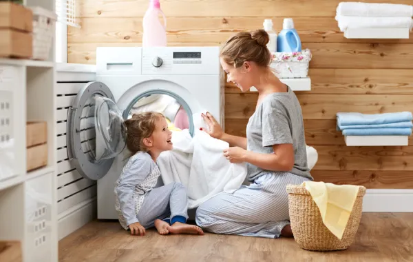 Foto madre e hija pequeña se miran sonriendo sentadas delante de la lavadora