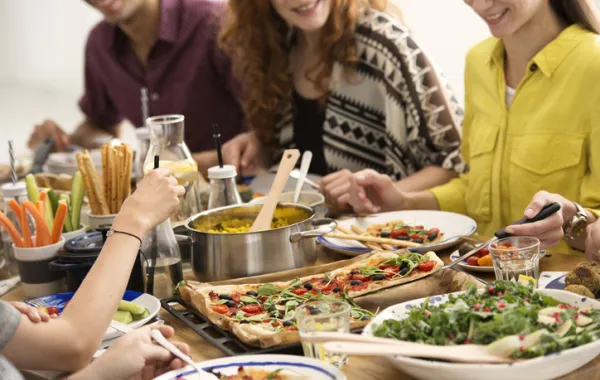 Foto de una mesa llena de comida vegetariana y rodeada de personas sonrientes