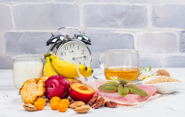 Foto de un selección de alimentos saludables acompañados por un reloj despertador antiguo