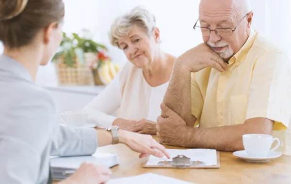 Foto de una pareja de personas mayores que leen una papel que les muestra una profesora