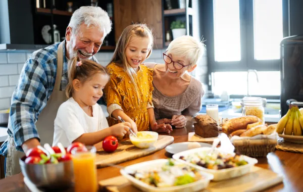 Foto de unos abuelos cocinando con sus nietos y sonriendo todos
