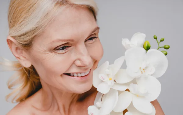Foto de una mujer adulta sonriendo mientras sostiene unas flores blancas