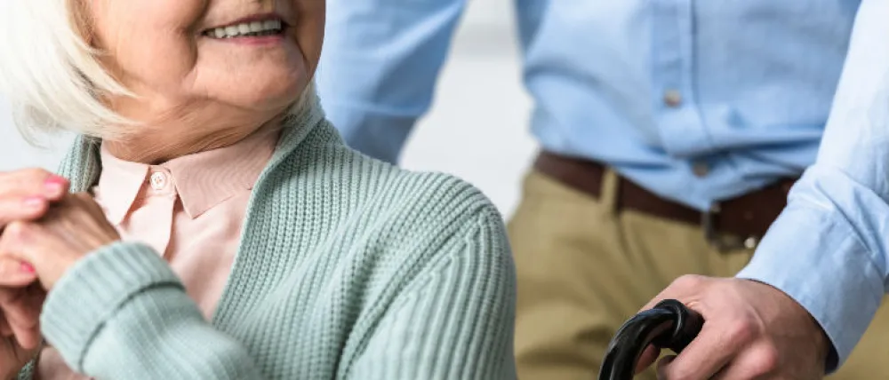 Foto de una señora mayor sentada en una silla de ruedas y sonriendo a la persona que le lleva