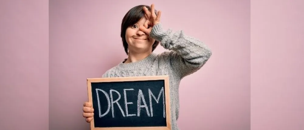 Foto de una chica con síndrome de down que sostiene una pizarra que pone sueño en inglés