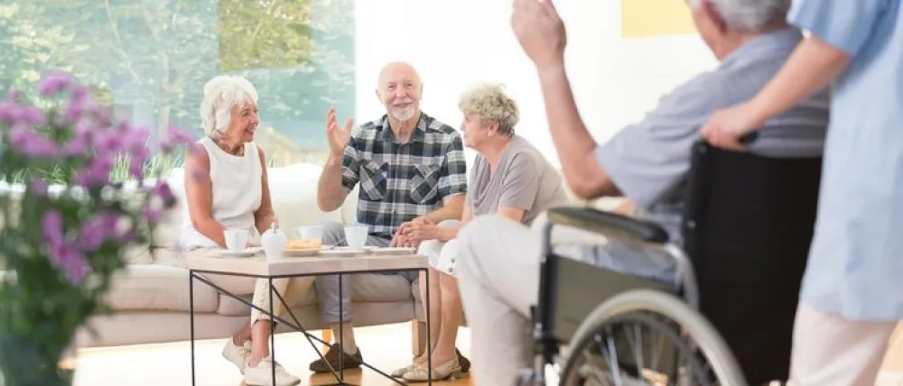 Foto de varias personas mayores sentadas charlando alegremente en un salon de una residencia