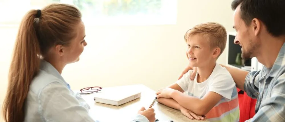Foto de un niño acompañado por su padre y hablando con una profesora