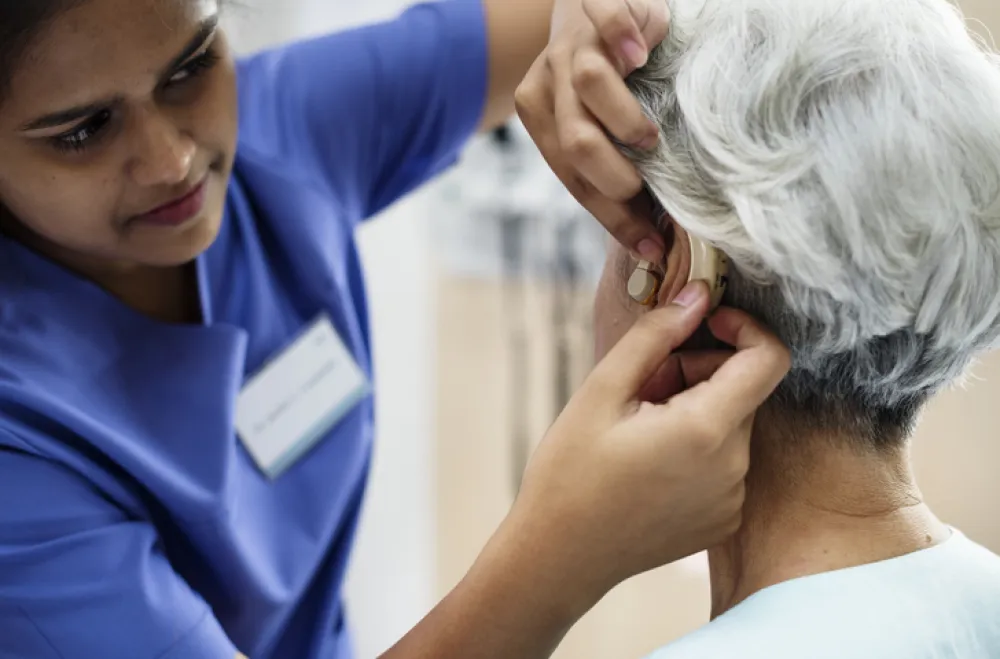 Foto de un sanitario ajustando al audífono a una señora