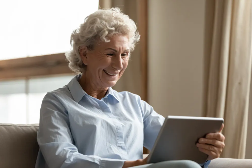 Foto de una señora mayor sonriendo mientras lee en una tablet