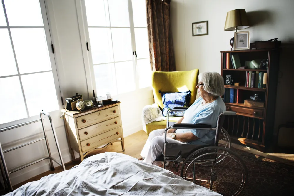 Foto de una mujer mayor en silla de ruedas que está sola en una habitación
