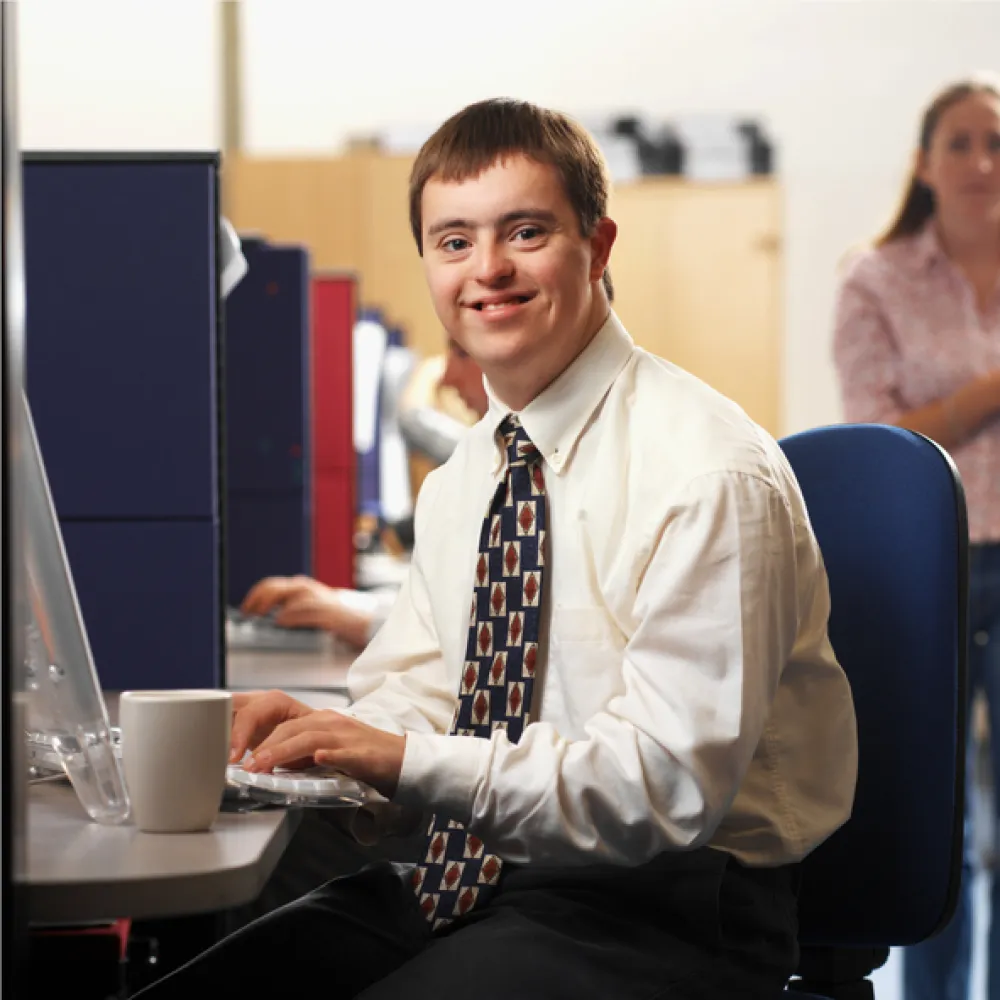 Foto de un joven con síndrome de down vestido con corbata y delante de un ordenador