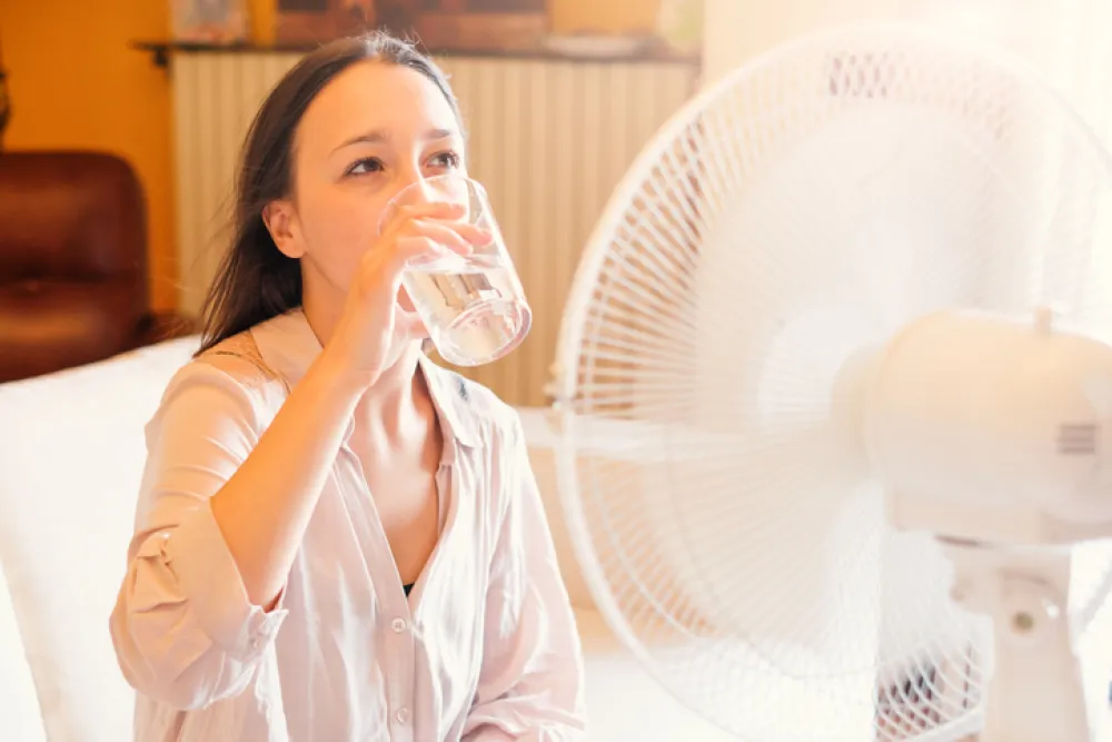 Foto de una mujer bebiendo agua frente a un ventilador