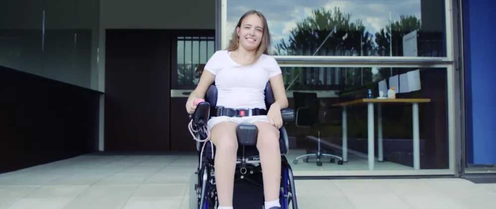 Foto de una chica joven en silla de ruedas delante de un edificio