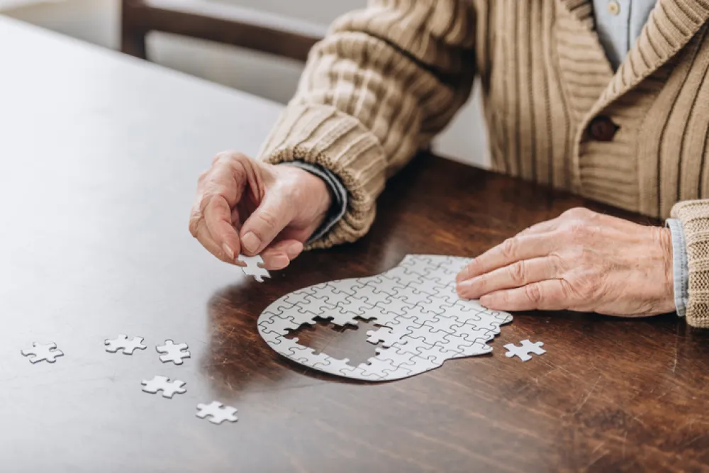 Foto de unas manos de persona mayor haciendo un puzle con forma de cabeza