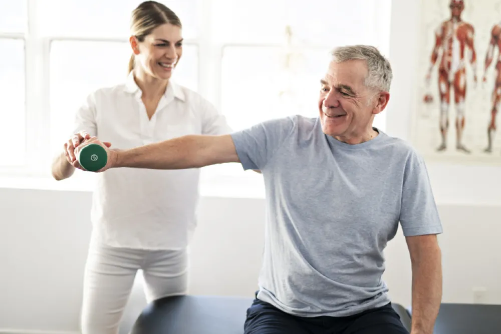 Foto de un señor adulto realizando ejercicios con el brazo con una fisioterapeuta