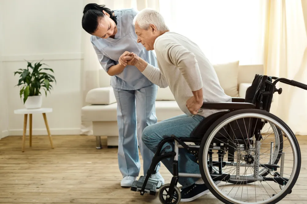 Foto de un hombre mayor levantandose en silla de ruedas ayudada por una enfermera