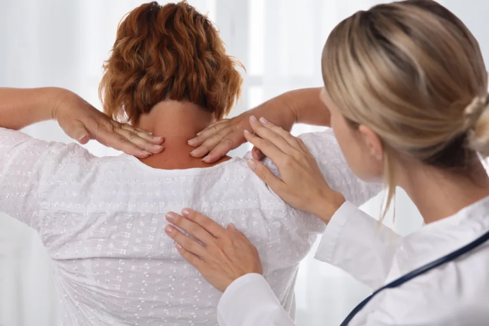 Foto de una mujer joven de espaldas atendida por una doctora que chequea su cuello y espalda